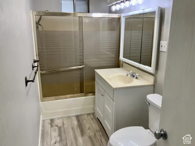 Vanity with an integrated sink, medicine cabinet with overhead lighting, wood-finish flooring, and a shower-tub combination with sliding glass doors