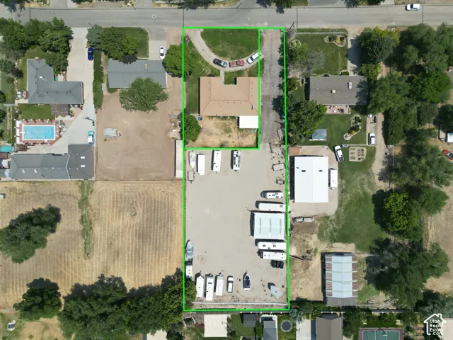 Expansive property encompassing multiple structures and a substantial open area, featuring a primary residence with an attached garage, a secondary structure with a light-colored roof, and a large gravel-surfaced lot