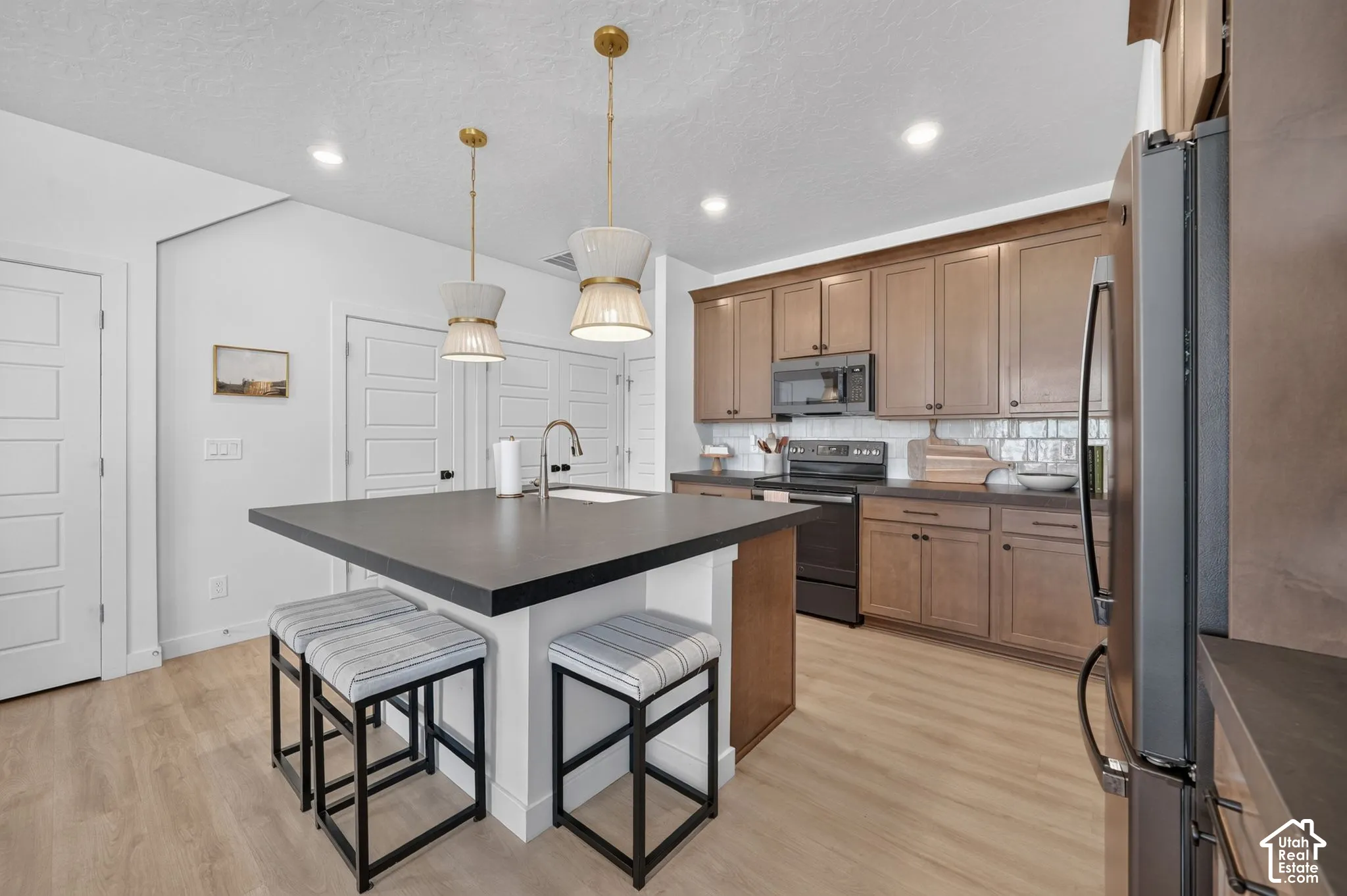Kitchen featuring a central island with a sink, pendant lighting, wood-finish flooring, and recessed ceiling lights