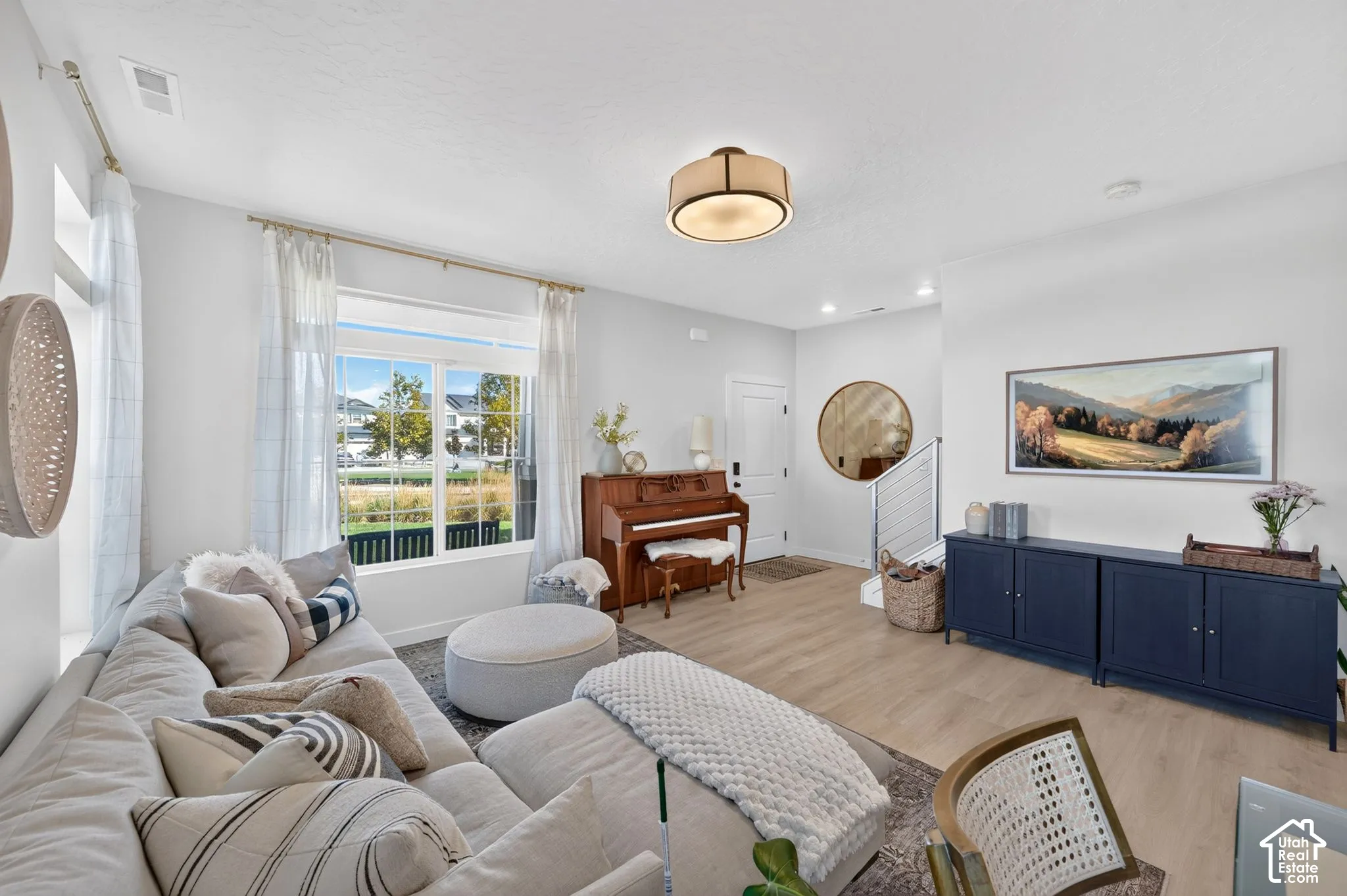 Recessed lighting, large window with ample natural light, wood-finish flooring throughout, and a built-in stair railing