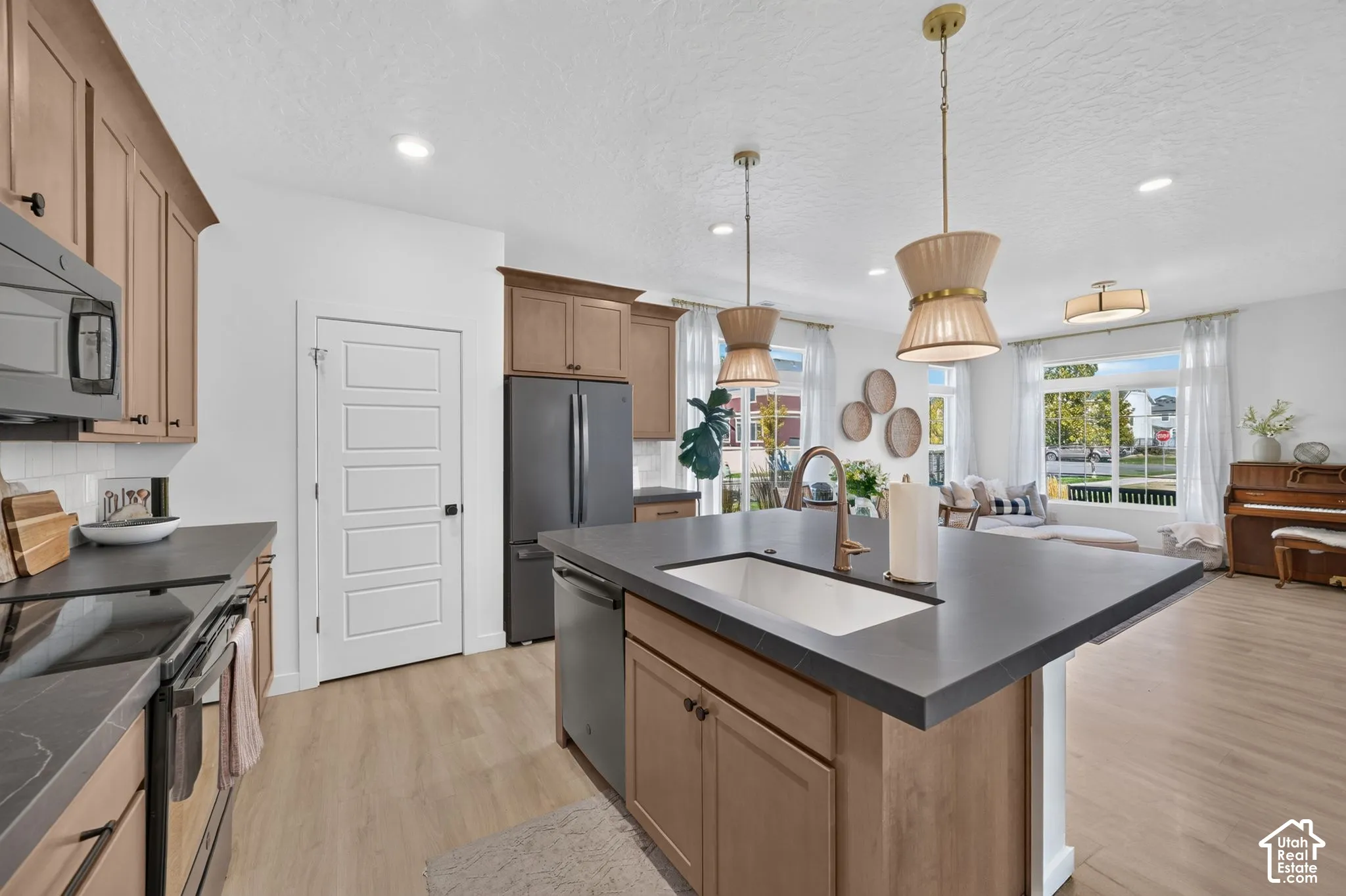 Kitchen featuring a large island with an undermount sink, pendant lighting, stainless steel appliances, and wood-finish flooring