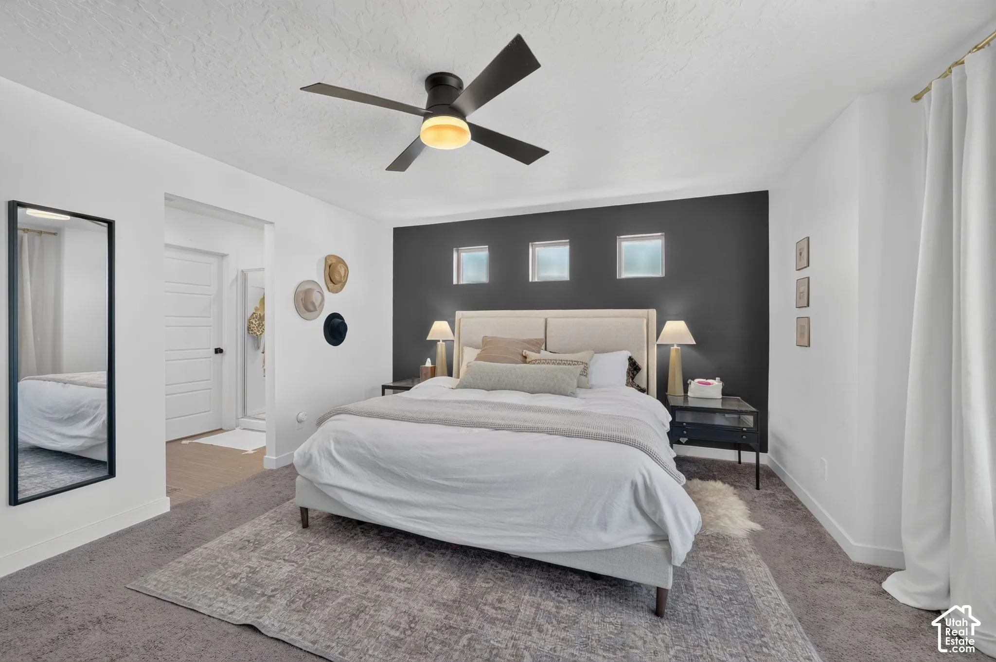 Carpeted flooring, ceiling fan, white paneled door, three transom windows, dark accent wall