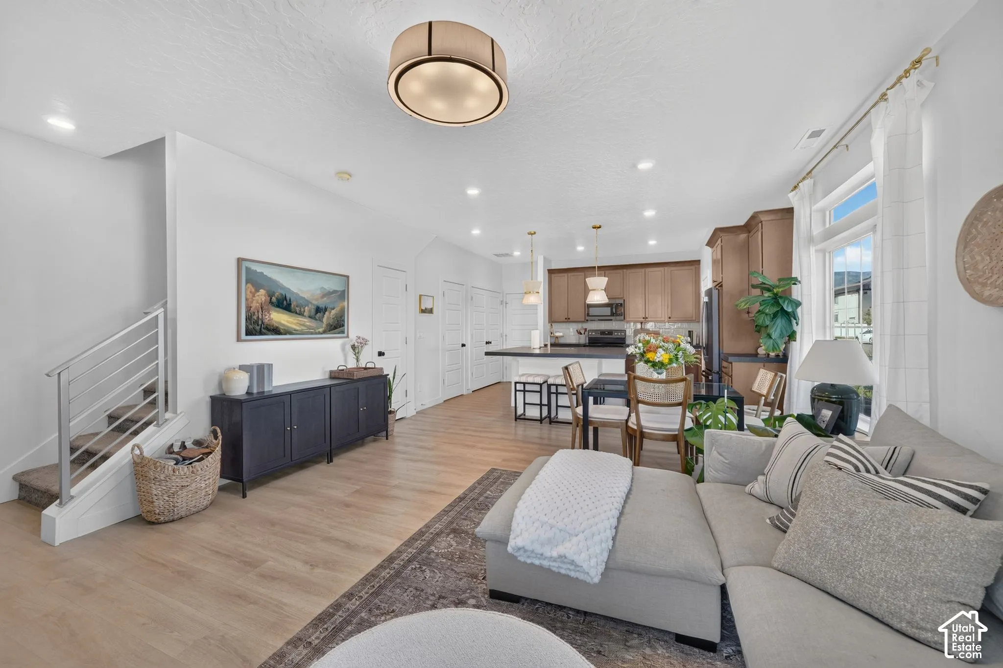 Open-concept living space featuring wood-finish flooring, recessed lighting, and a modern staircase with metal railings