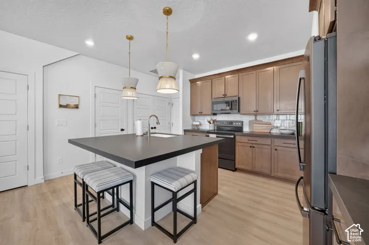 Kitchen featuring a central island with a sink, pendant lighting, wood-finish flooring, and recessed ceiling lights