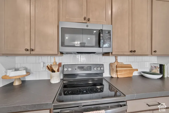 Modern kitchen featuring light wood-finish cabinetry, stainless steel microwave, black electric range, and solid surface countertops