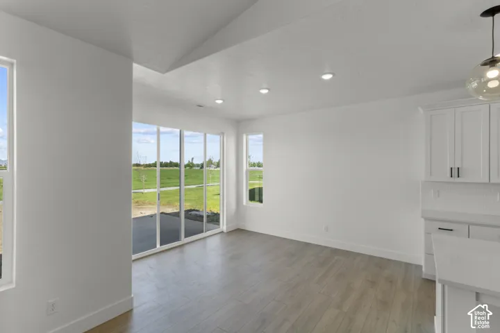 Expansive sliding glass doors, recessed lighting, wood-finish flooring, white cabinetry, and a pendant light fixture