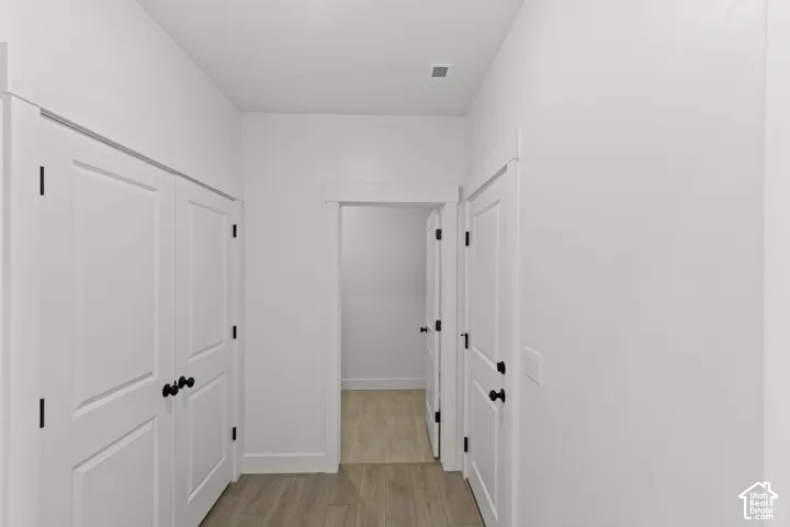 Hallway featuring white panel doors, black hardware, and wood-finish flooring