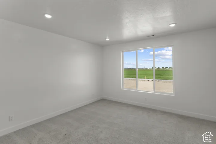 Recessed lighting, light-toned carpeting, white walls, and a large window with a distant green field