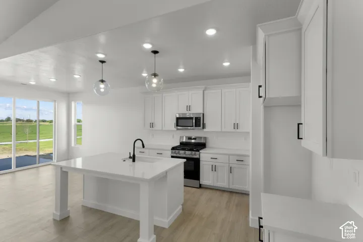 Modern kitchen featuring white shaker cabinetry, stainless steel appliances, a center island with sink, wood-finish flooring, and pendant lighting