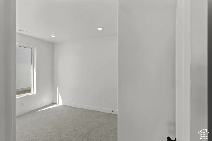 Recessed ceiling lighting, white walls, gray carpeting, and a single window with blinds