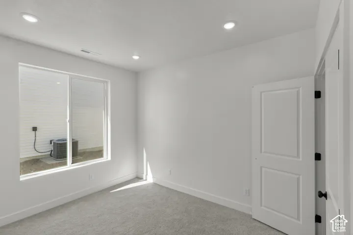 Recessed ceiling lighting illuminates a room with light gray carpeting and white walls