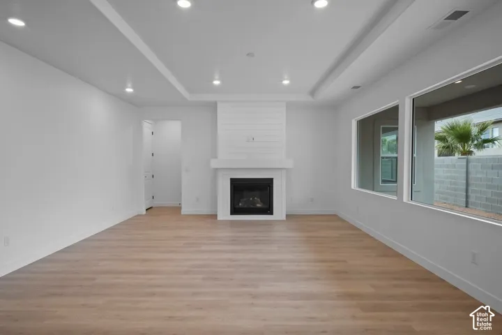 Open living area with wood-finish flooring, a contemporary fireplace with shiplap detailing, recessed lighting, and large rectangular windows