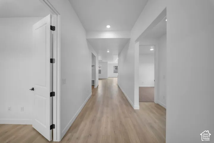 Hallway featuring wood-finish flooring, recessed lighting, white panel doors with black hardware, and crisp white walls