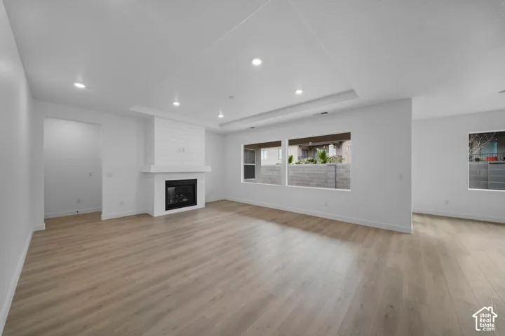 Recessed lighting, wood-finish flooring, fireplace with shiplap detail, tray ceiling, and multiple windows