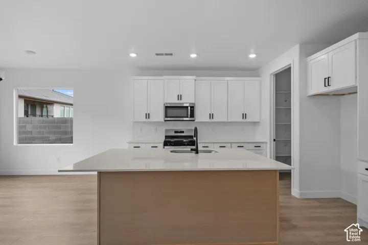 Kitchen featuring an island with a light-toned wood-finish base, light-colored countertop, and a stainless steel oven