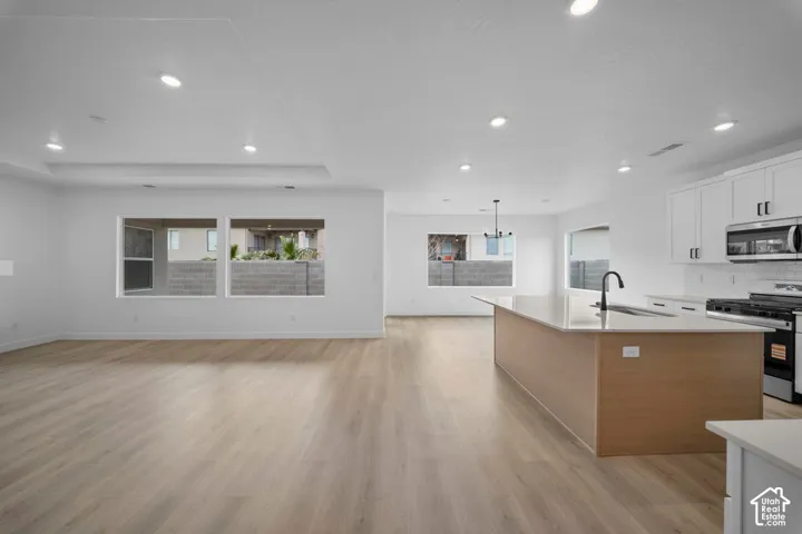 Recessed lighting illuminates the open-concept living space, featuring wood-finish flooring and a kitchen with white cabinetry, stainless steel appliances, and a central island with a sink