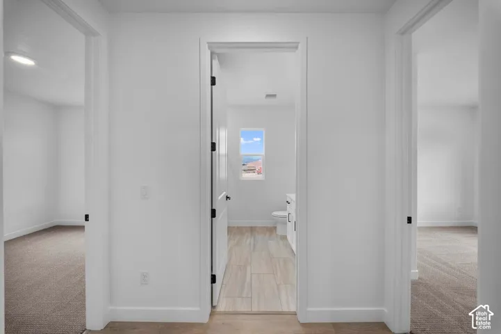 Hallway featuring white walls, wood-finish flooring, and black hardware