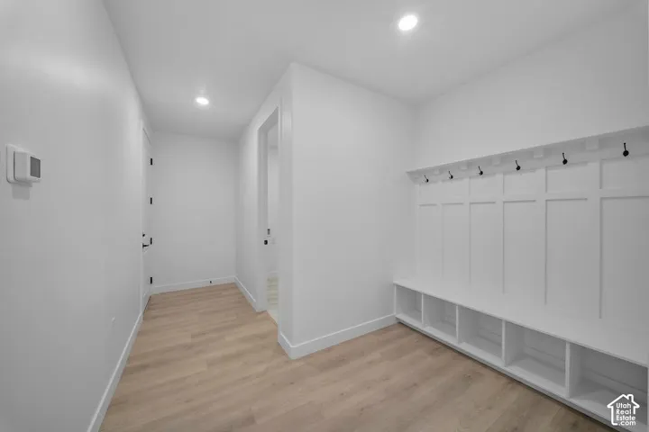 Built-in storage bench with cubbies, board and batten wall paneling, matte black coat hooks, light wood-finish flooring, and recessed lighting