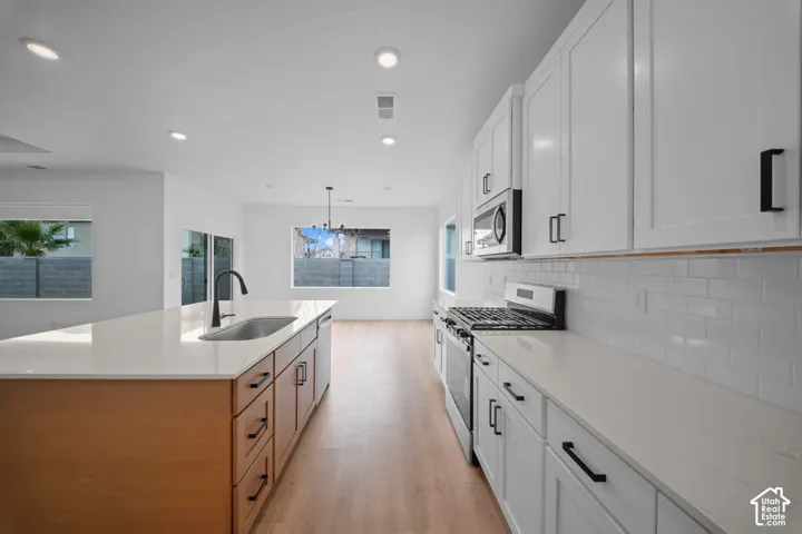White shaker cabinetry, light wood-finish flooring, recessed lighting, subway tile backsplash, and a kitchen island with an undermount sink