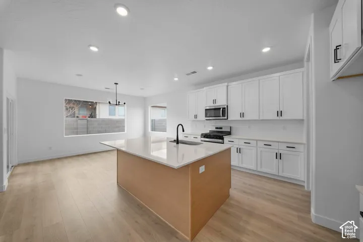 Open-concept kitchen featuring an island with a light-toned countertop, white cabinetry with dark hardware, a stainless steel microwave, and wood-finish flooring