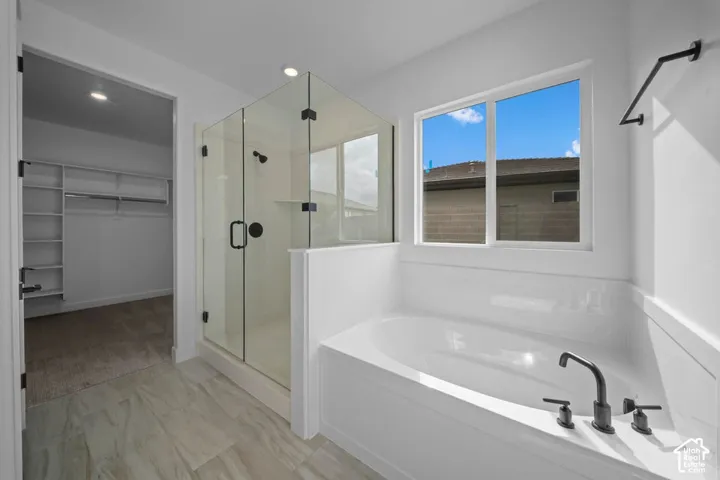 Spacious bathroom featuring a built-in soaking tub with a matte black faucet, a glass-enclosed shower with a matte black shower head, and light-toned tile flooring