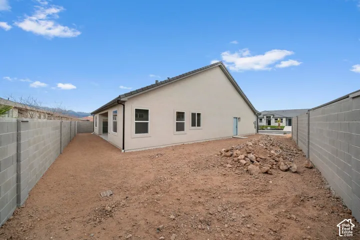 Expansive backyard with a stucco exterior, multiple windows, a rear door, and block wall perimeter fencing