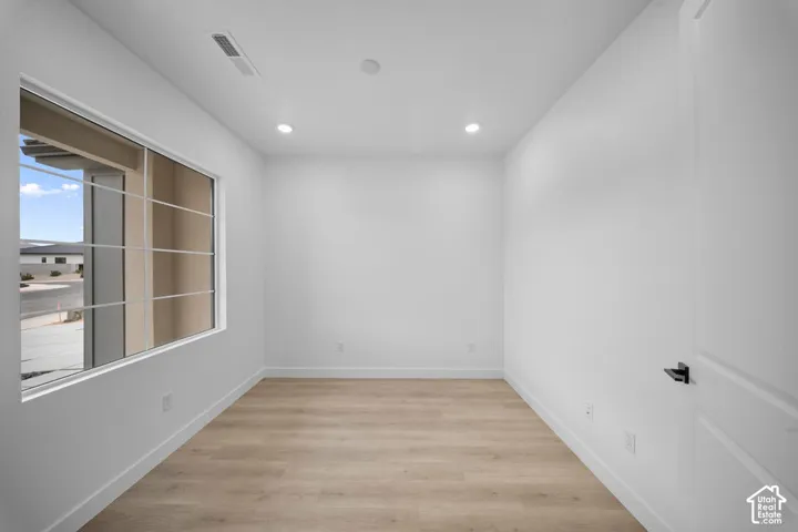 Recessed ceiling lighting, light wood-finish flooring, white walls, white trim, and a white interior door with black hardware
