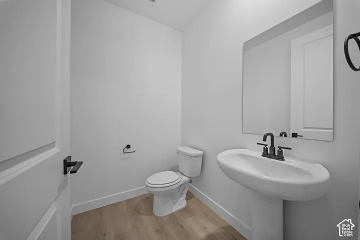 Pedestal sink with dark-finished faucet, rectangular wall mirror, and wood-finish flooring