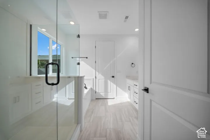 Glass-enclosed shower, built-in bathtub, dual vanity with undermount sinks, recessed lighting, and large windows