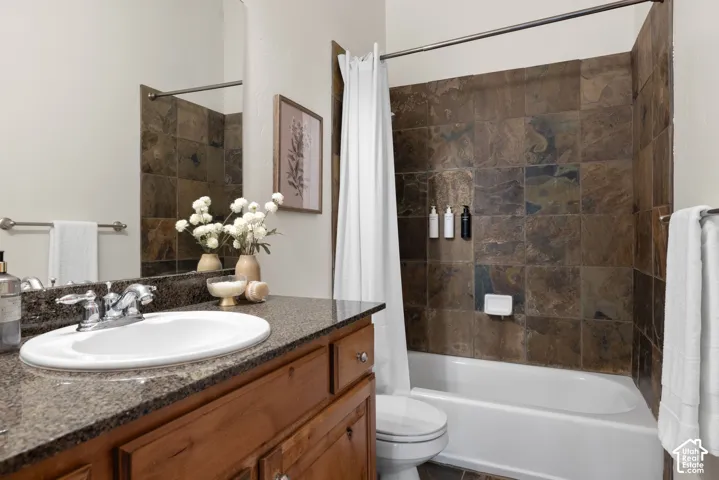 Bathroom featuring a built-in bathtub with tiled surround, a vanity with an integrated sink, a dark stone-finish countertop, and wood-finish cabinetry