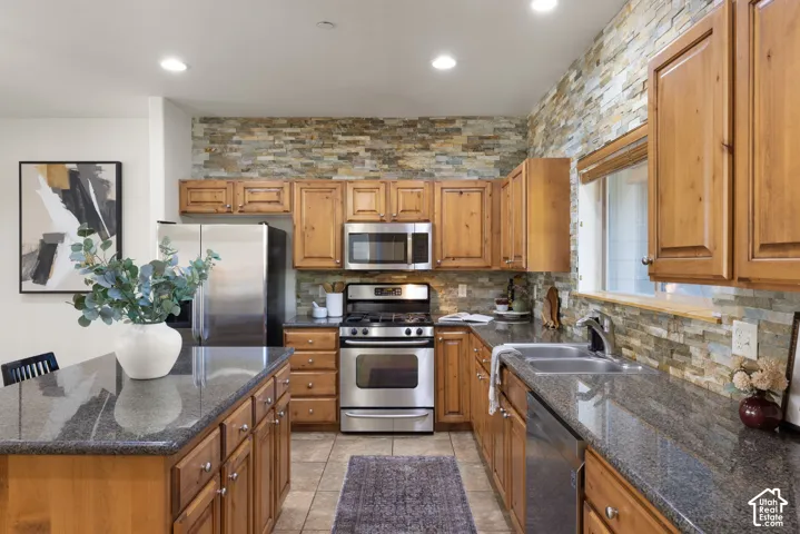 Kitchen featuring wood cabinetry, stainless steel appliances, granite countertops, a stone-finish accent wall, and tile flooring