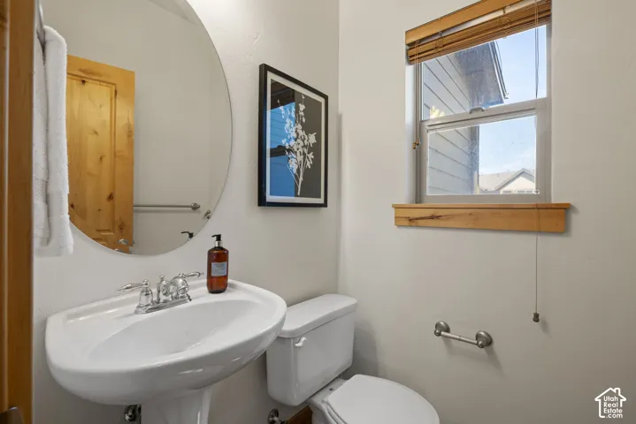 Pedestal sink with chrome fixtures, oval mirror, and a window with a wooden sill