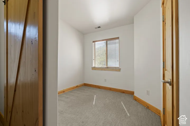 Spacious bedroom featuring warm wood-trim detailing, neutral carpet flooring, and abundant natural light from a large window with plantation shutters