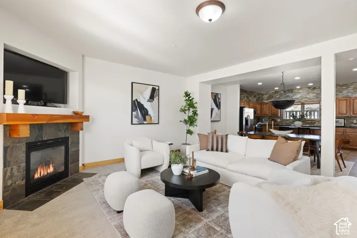 Stone-tiled fireplace with a wood mantle, recessed television alcove, overhead lighting fixture, and a kitchen featuring wood cabinetry and stone-tiled backsplash