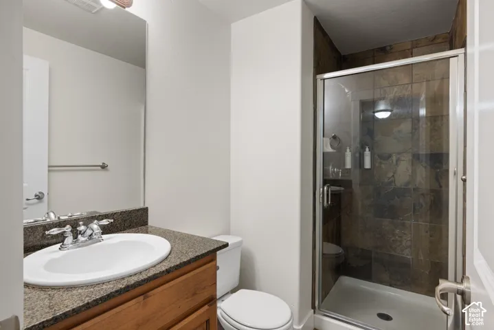 Bathroom featuring a wood-finish vanity with a built-in sink, stone-finish countertop, and a glass-enclosed shower with tiled walls