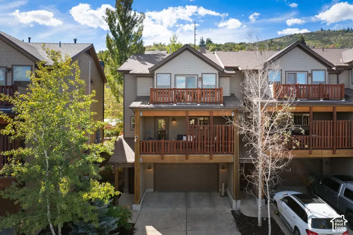 Multi-level townhome exterior featuring an attached garage, two private balconies with wood railings, and a covered entry