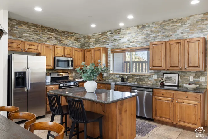 Kitchen featuring natural wood cabinetry, stone-clad walls, recessed lighting, stainless steel appliances, and a central island with a stone countertop