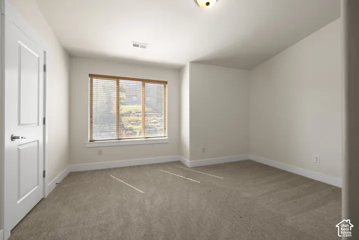 Neutral wall tones with a window featuring wood-finish blinds, carpet flooring, a flush-mount ceiling light, and a white paneled door with brushed nickel hardware