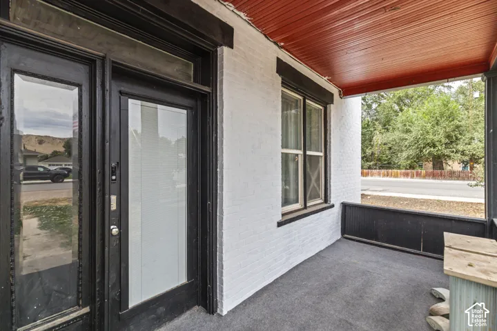 Porch featuring painted brick exterior, dark-stained wood ceiling, and a glass-paneled entry door