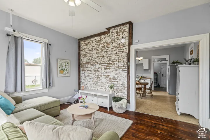 Exposed brick accent wall, wood-finish flooring, ceiling fan, and window with natural light