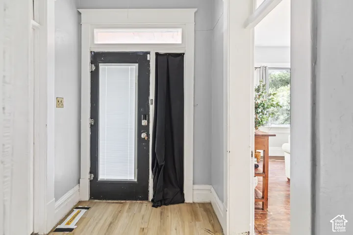Wood-finish flooring with a black door featuring a transom window, sidelight, and white trim