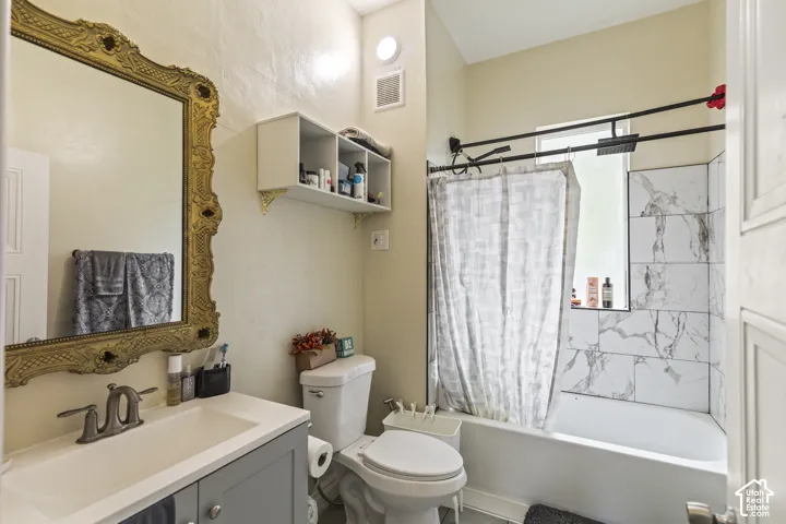 Bathroom featuring a single vanity with storage, a decorative framed mirror, a built-in shelving unit, and a shower-tub combination with large format tiled walls and a rainfall showerhead