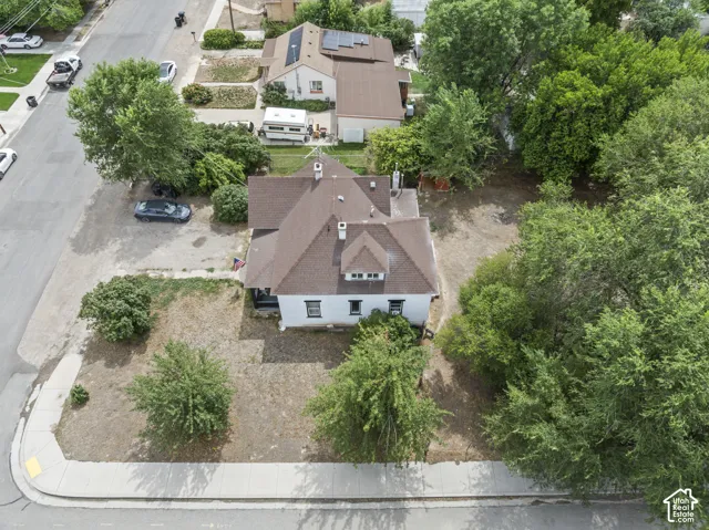 White exterior with brown shingle roof, established landscaping, and mature trees
