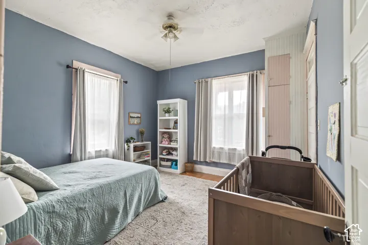 Room featuring dual windows with sheer and opaque drapery, a ceiling fan with integrated lighting, and a built-in storage unit with paneled doors