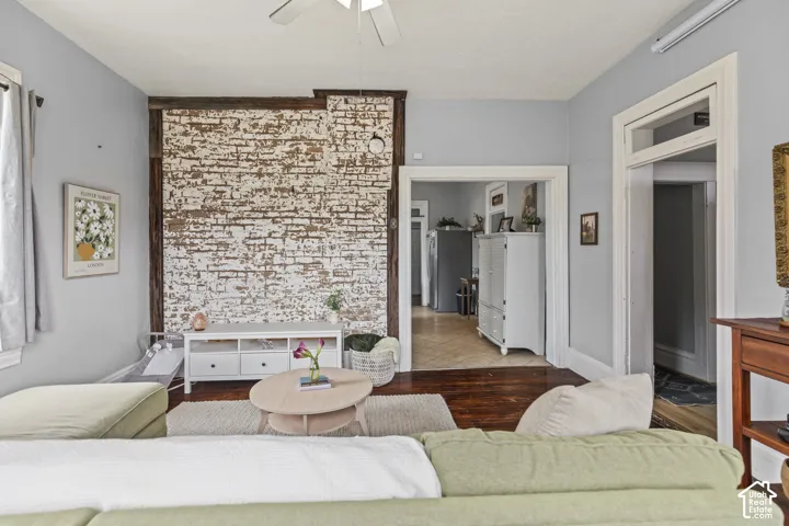 Exposed brick accent wall, wood-finish flooring, ceiling fan, and white trim around doorways