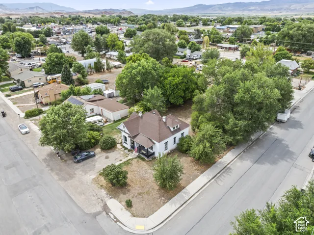 Corner lot property featuring a white exterior, dark-toned roof, and mature trees