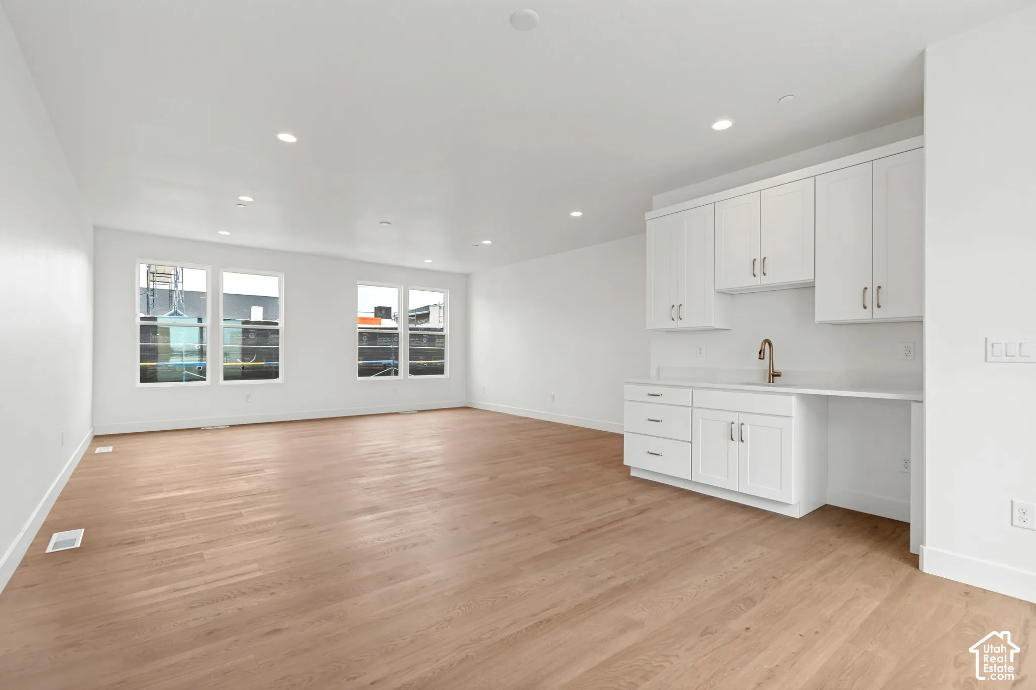Light wood-finish flooring, recessed lighting, multiple windows, white cabinetry with a built-in sink, and a contrasting faucet