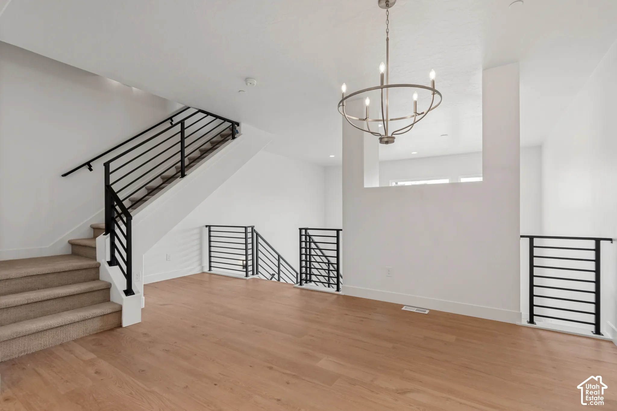 Carpeted staircase with black metal railing, wood-finish flooring, and a contemporary chandelier