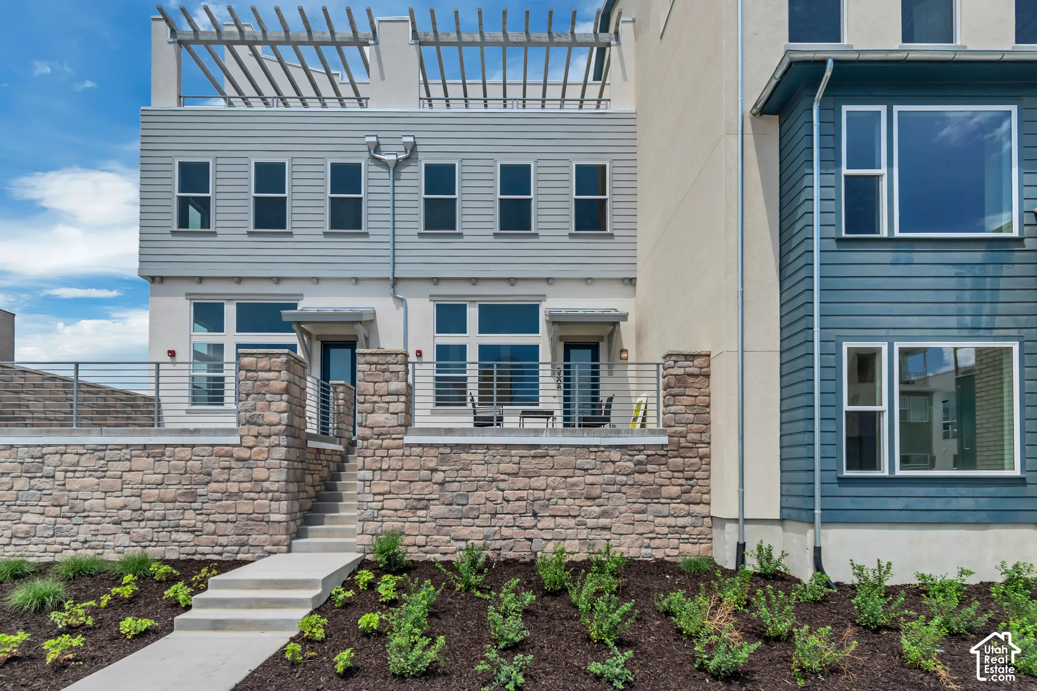 Contemporary multi-level exterior with a stone-clad retaining wall, horizontal siding, and a rooftop pergola
