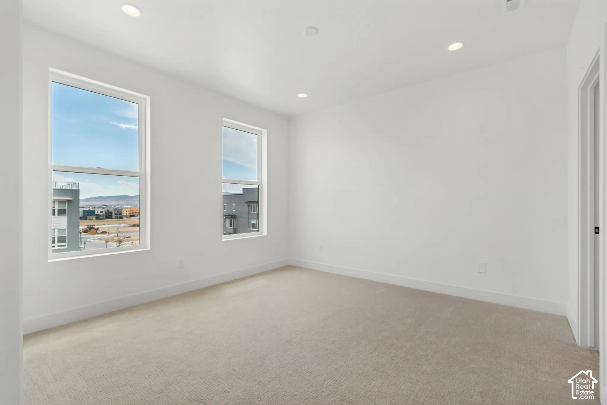 Neutral-toned carpeting, recessed ceiling lighting, and two large windows with white trim